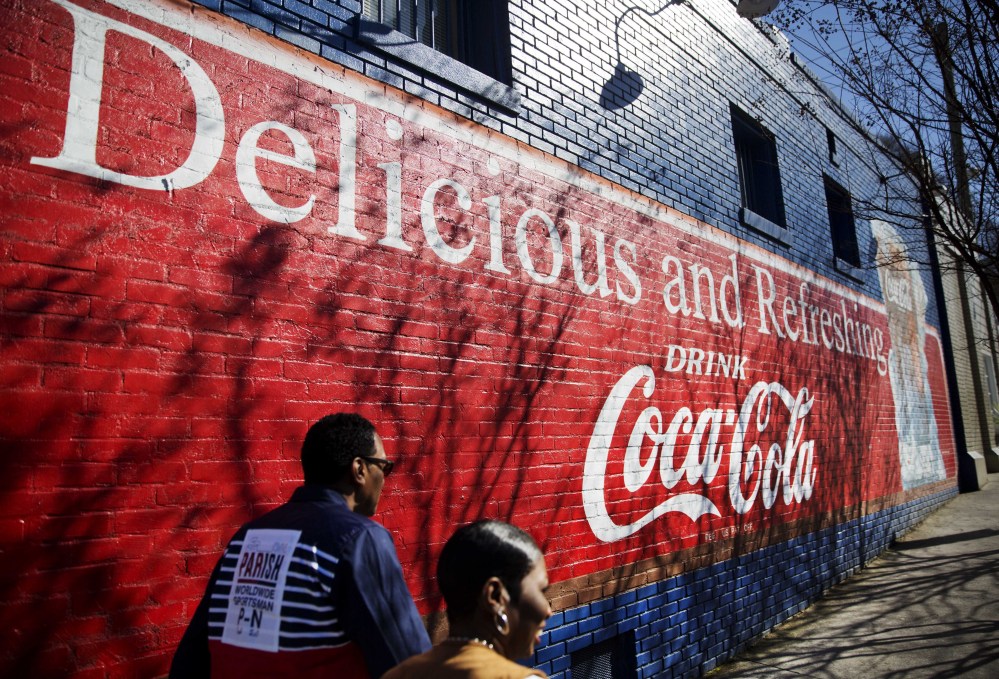 A mural advertising Coca-Cola decorates the side of a building as pedestrians pass Thursday in Atlanta. Coke and Pepsi are trying to rehabilitate soda’s cheap image in an effort to fetch higher prices.