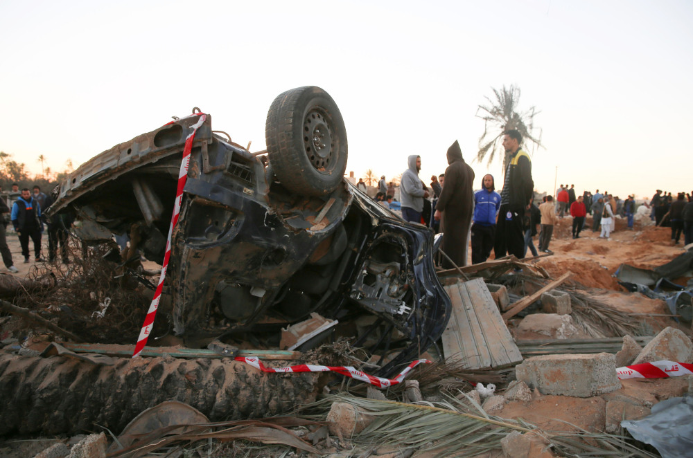 People gather by the wreckage of a car after an airstrike Friday on a house and training camp belonging to the Islamic State group, west of Sabratha, Libya.