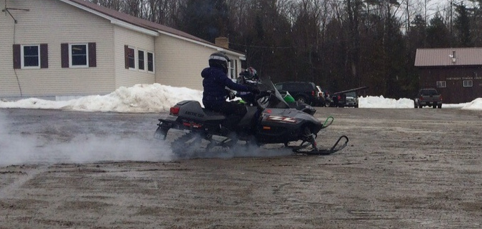 Snowmobilers ride from a parking lot outside the Northern Timber Cruisers Clubhouse, which usually is full of snow. A lack of snow and ample rain has left nothing but mud.