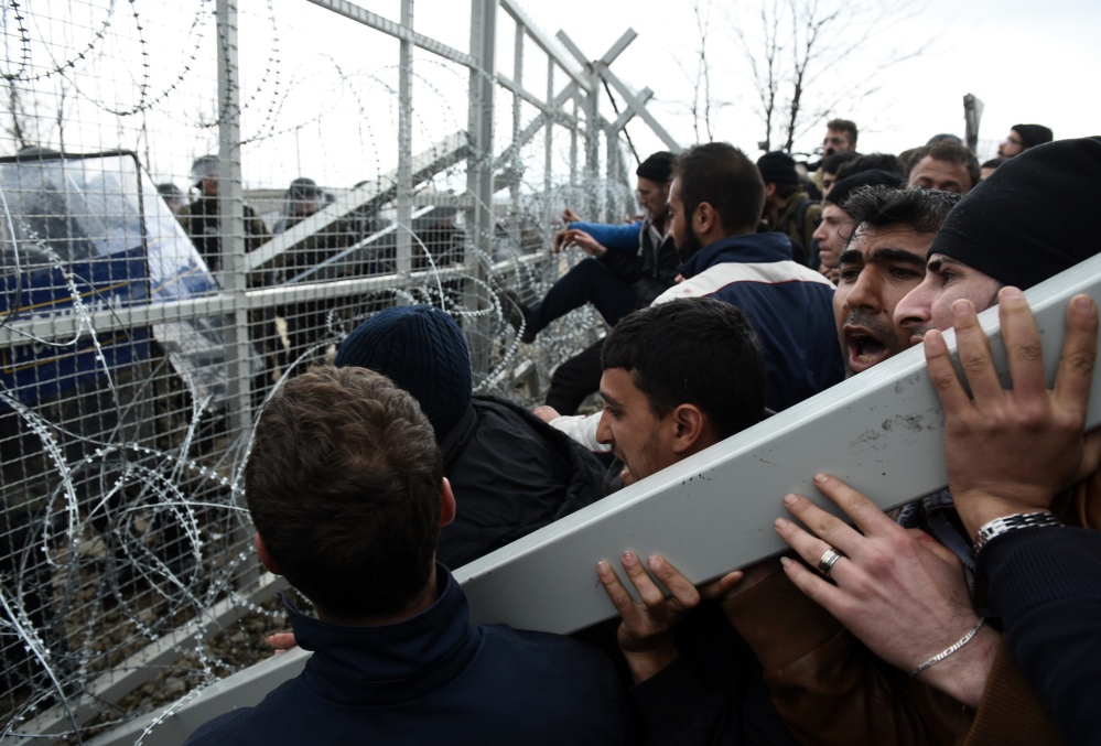 Refugees and migrants try to break an iron fence from the Greek side of the border as Macedonian police stand guard, near the northern Greek village of Idomeni on Monday. Macedonian police fired tear gas and stun guns as several hundred Iraqi and Syrian refugees, frustrated at days of delays in crossing the Greek-Macedonian border, broke down a gate on a nearby rail crossing.