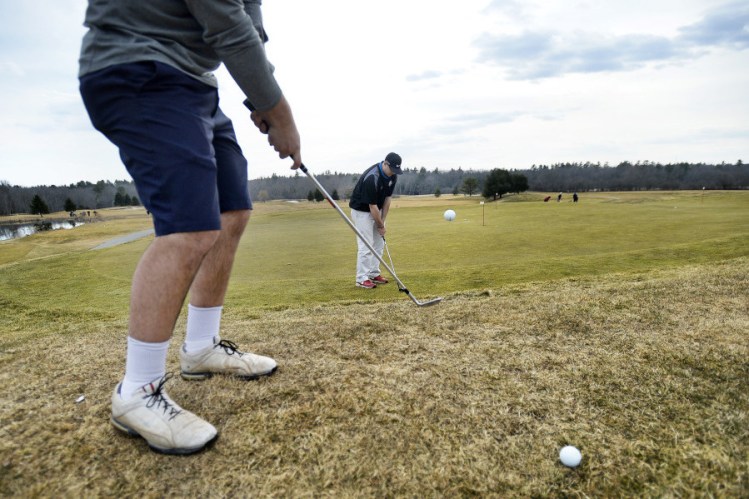 Mike Steinberg of Falmouth, in shorts, chips past golfing partner Jake Lachance of Falmouth onto the putting green at Nonesuch River Golf Club in Scarborough. More than 200 golfers played the course Wednesday, said General Manager Dan Hourihan.
