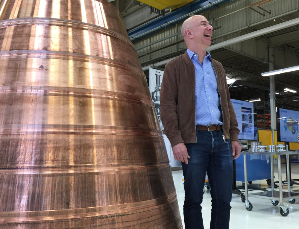 Amazon.com founder Jeff Bezos stands next to a copper exhaust nozzle to be used on a space ship engine, during tour of Blue Origin, in Kent, Wash. At left, Blue Origin team members ready the New Shepard Crew Capsule during assembly in Kent, Washington.