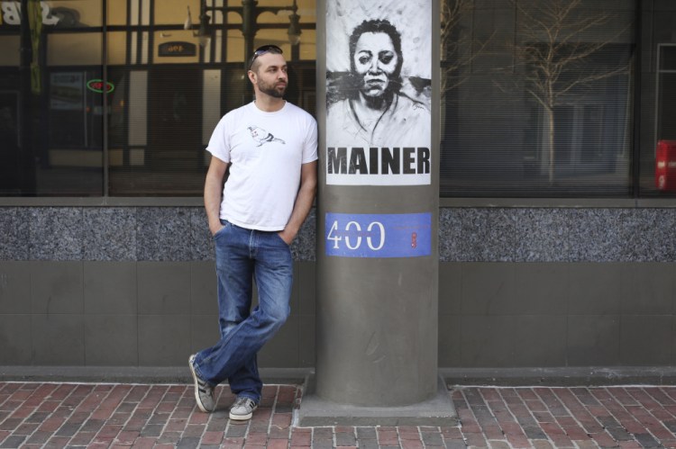 Street artist Orson Horchler, who goes by the name Pigeon, stands by posters he designed for the exhibition “400 Years of New Mainers” at the Maine Historical Society in Portland. 