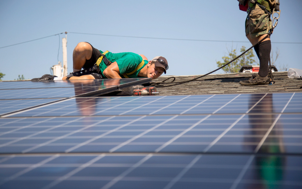 A SolarCity Corp. employee checks solar panels on the roof during an installation at a home in Kendall Park, New Jersey, last summer. The growth of private solar power will cost large scale generators about $2 billion this year.