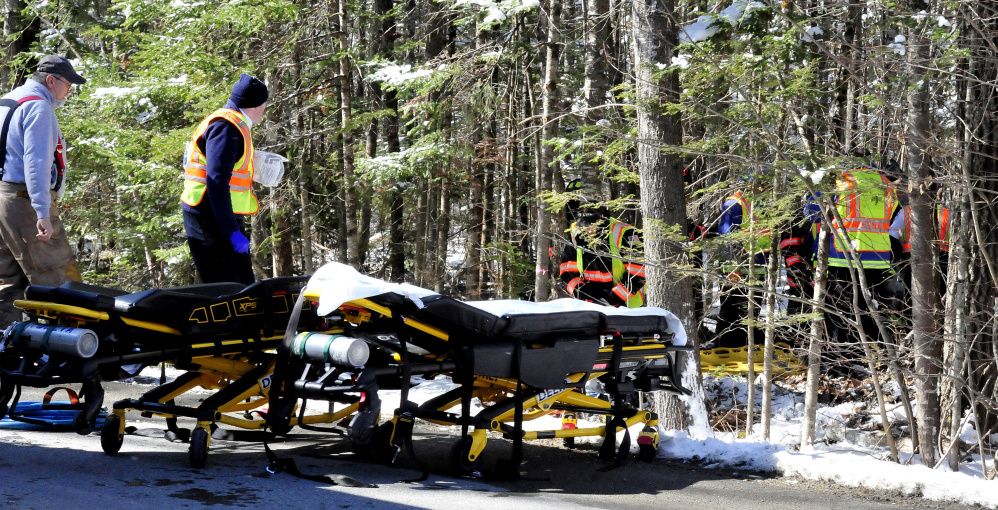 Firefighters wait beside gurneys as other firefighters free three victims from the wreckage of a car that landed in the woods Tuesday off Hanscom Road in Benton.