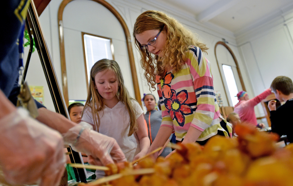 Fifth-graders Savanna Scalin, 11, right, and Eva Bardin, 10, get their skewers of roasted parsnips and carrots for a lunch taste-test at Albert S. Hall School in Waterville Wednesday