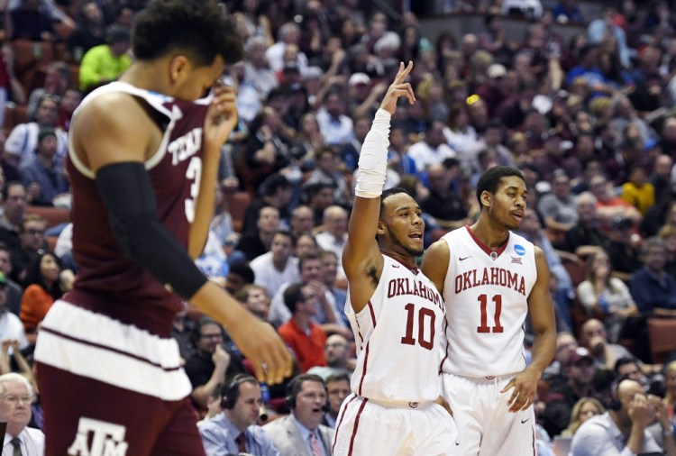 Oklahoma guard Isaiah Cousins (11) and guard Jordan Woodard celebrate as Texas A&M guard T.J. Distefano wipes his face during the second half of Oklahoma’s win Thursday night in the regional semifinals of the NCAA Tournament.