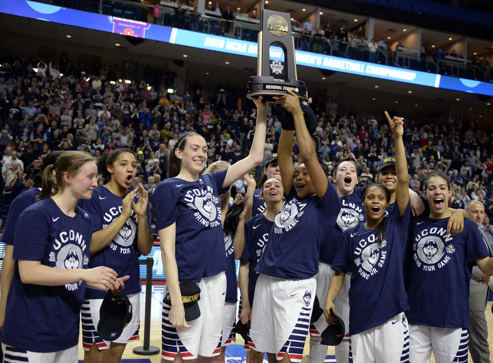 Connecticut’s Breanna Stewart, left, and Morgan Tuck celebrate with the trophy and teammates after winning 86-65 over Texas in their regional final Monday night in Bridgeport, Conn.