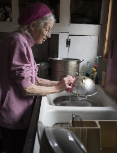 Joan McMurray washes her dishes by hand using rainwater from her roof that she catches in a barrel and then heats on a stove.