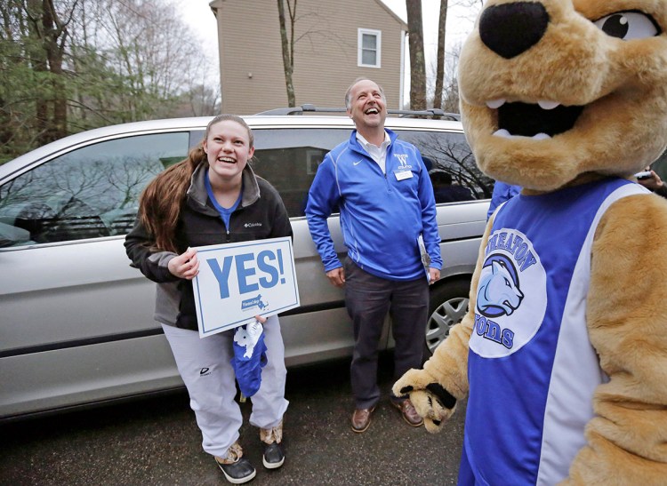 Maya Wolf, 17, holds a sign to her mother, not shown, from the driveway of their home in Franklin, Mass., during a  visit by Wheaton College President Dennis Hanno, center, and the school's mascot. The Associated Press