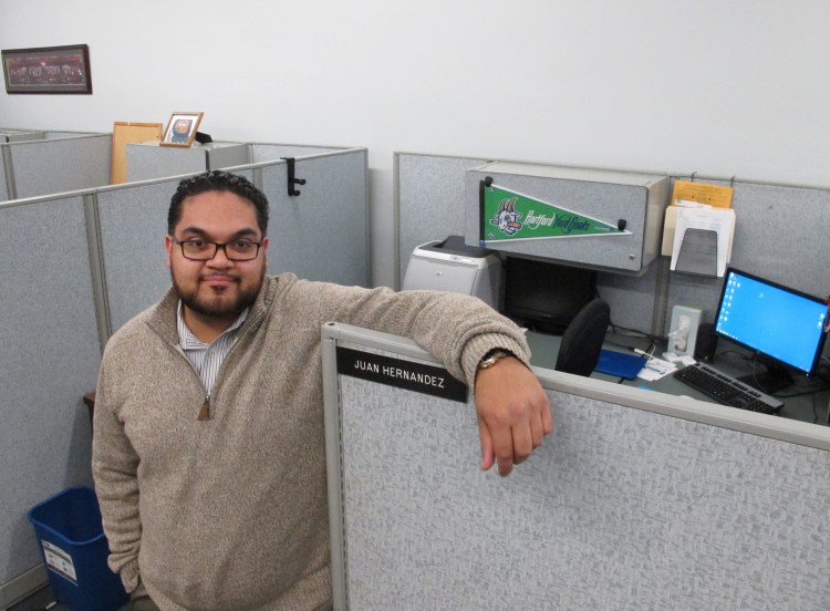 Juan Hernandez poses at his work cubicle in Hartford City Hall. Hernandez, 25, is among millennials nationwide with student debt who are worried about being able to qualify for a loan and come up with a down payment for a home.    The Associated Press