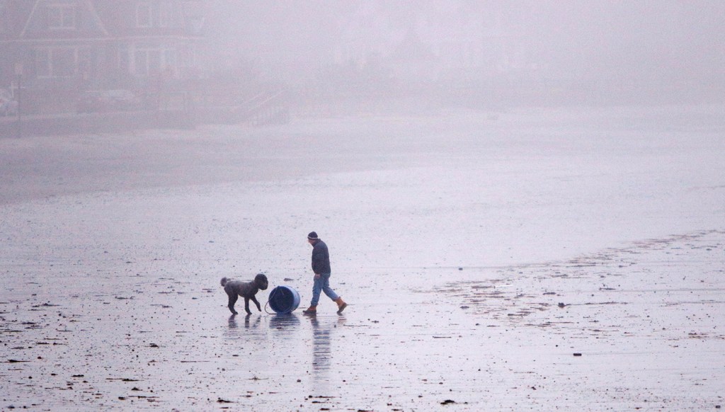 David Jones of Kennebunk rolls a bait barrel up to the sea wall at Gooch's Beach in Kennebunk while walking his dog Fritz at the beach.  The barrel had washed ashore overnight and the high tide at midnight resulted in some splash over that created minor flooding along parts of the coast. 