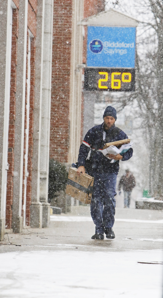 Biddeford letter carrier James Dolloff carries mail and packages along Main Street on his way to a delivery at the McArthur Library as snow falls Monday.