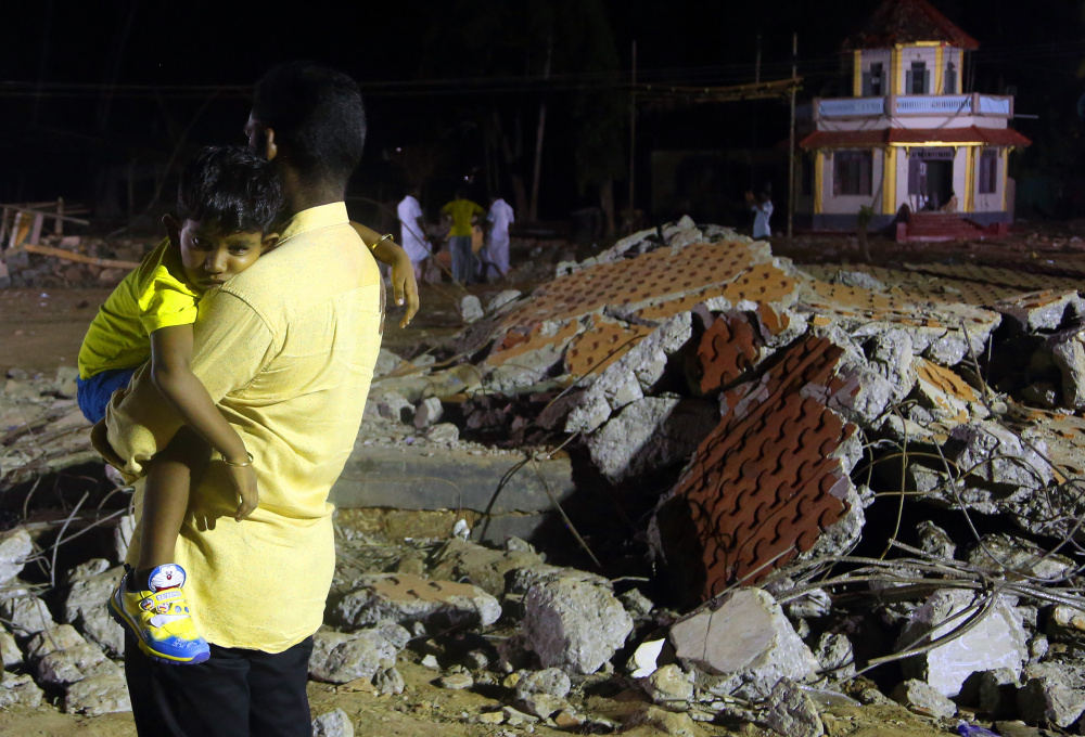 A man carries his child past the debris of a damaged building where a massive fire broke out during a fireworks display at the Puttingal temple complex in Paravoor, India.