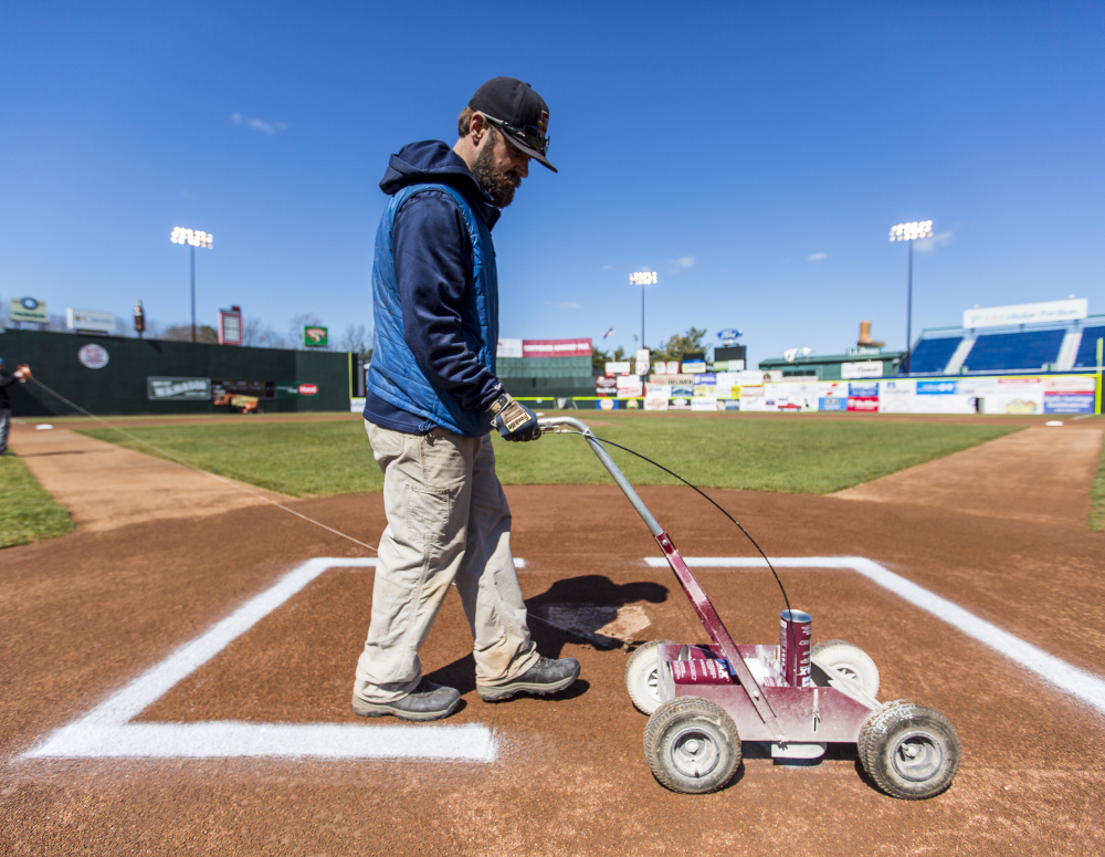 Jason Cooke, the assistant groundskeeper at Hadlock Field, paints the batters' boxes in preparation for Thursday night's home opener.