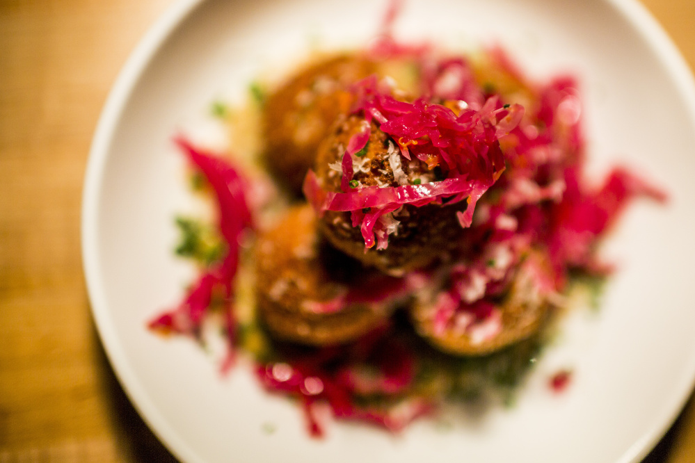 The arancini rest on eggplant puree and are topped with pickled cabbage.