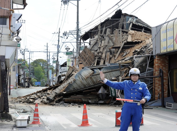 A police officer stands guard in front of a house destroyed by an earthquake in Mashiki, Kumamoto prefecture, southern Japan, Saturday.
