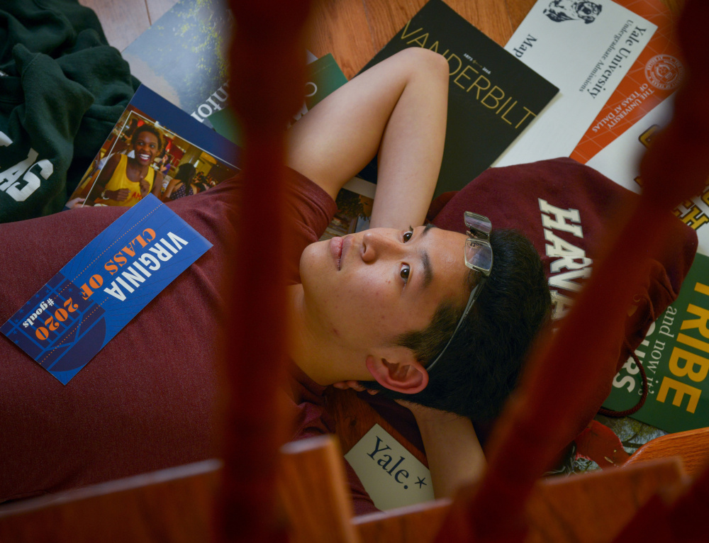 Apollo Yong, 17, reclines on a bed of college paraphernalia at home in Arlington, Va. A strong candidate, he nevertheless is among thousands placed on college wait lists.