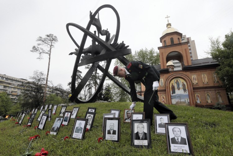A soldier places portrait photos near the monument erected in memory of the victims of the Chernobyl explosion in Ukraine's capital Kiev, Ukraine, Tuesday.