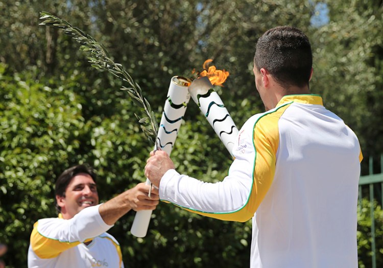 Former Brazilian volleyball player Giovane Gavio, left, receives the Olympic flame by Greek gymnast Eleftherios Petrounias, right, after the ceremonial lighting of the Olympic flame in Ancient Olympia, Greece.