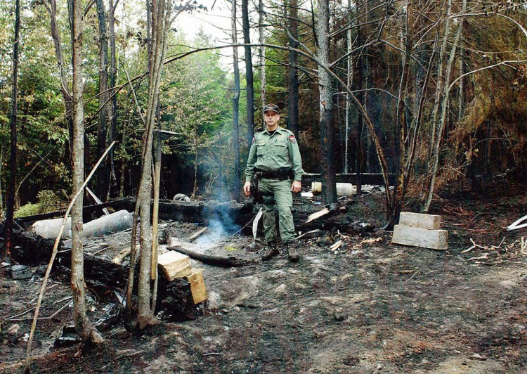 An officer for the Maine Department of Inland Fisheries &  Wildlife stands where a fire set by fleeing workers burned an area in a forest where authorities seized $9 million worth of marijuana in Township 37. Three men convicted in the enterprise were given sentences ranging from 5 to 14 years Thursday in U.S. District Court in Bangor.