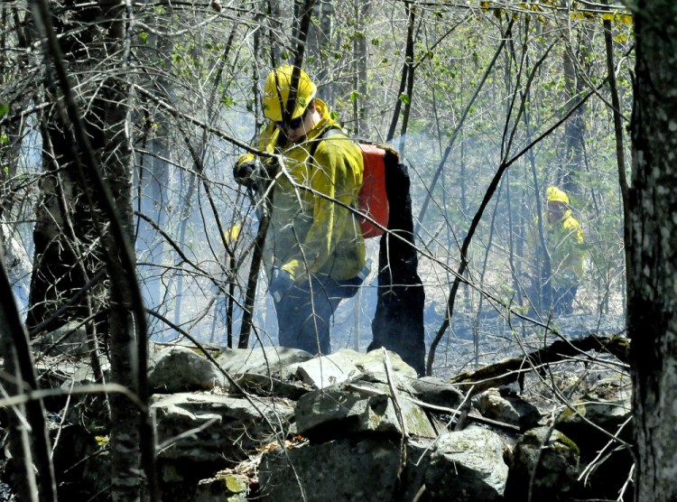 Wilton firefighter Brett Osgood uses a portable water tank to fight a wind-driven woods fire Wednesday on Route 43 in Starks. Numerous area fire departments showed up to put out the flames. Fire danger has been higher than normal this spring in central Maine.
