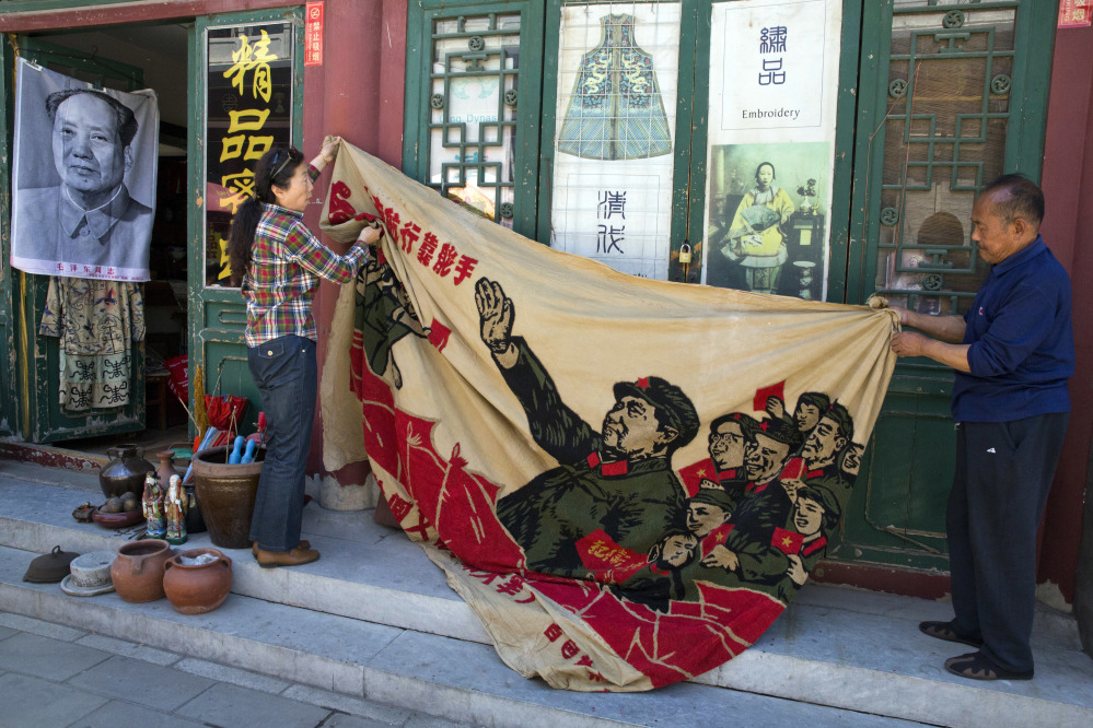 Vendors unfurl a banner from 1969 depicting former Chinese leader Mao Zedong as he "inspects the great army of the Cultural Revolution" with the slogan "Navigating the seas depends on the helmsman" at a curio market in Beijing on Monday.