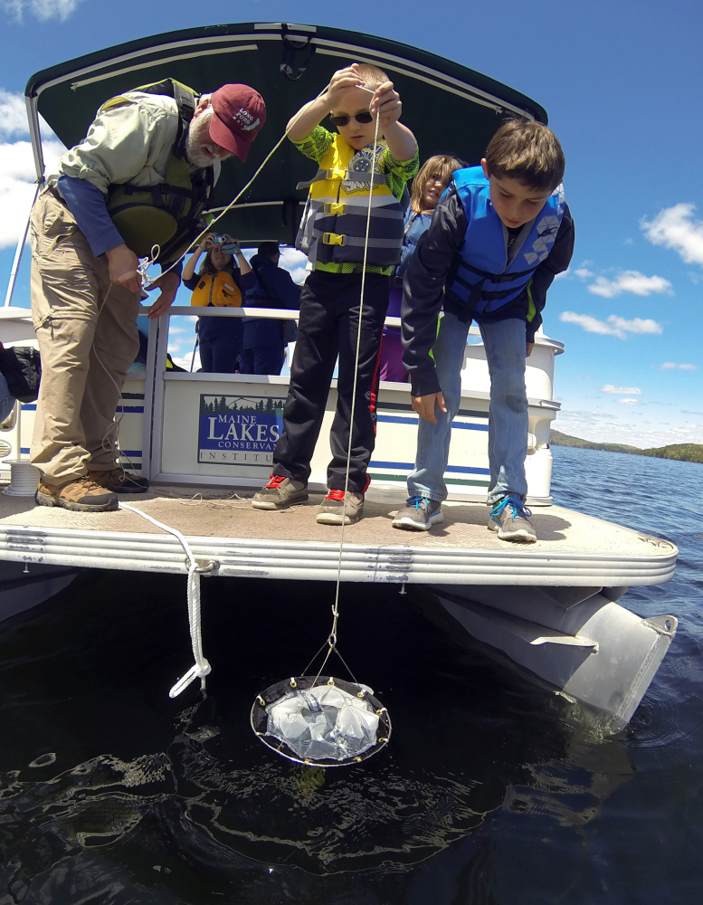 Peter Kallin, left, Noah Easter and Cobey Dunn drop a net to collect plankton Wednesday on board the Maine Lakes Society's floating classroom on Great Pond in Belgrade.