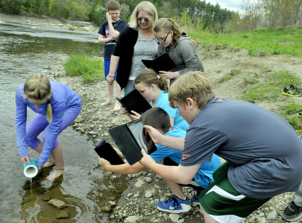 Teacher Patricia Dunphy, center, watches as students photograph Peyton Estes releasing salmon fry into Sandy River in Norridgewock on Thursday.