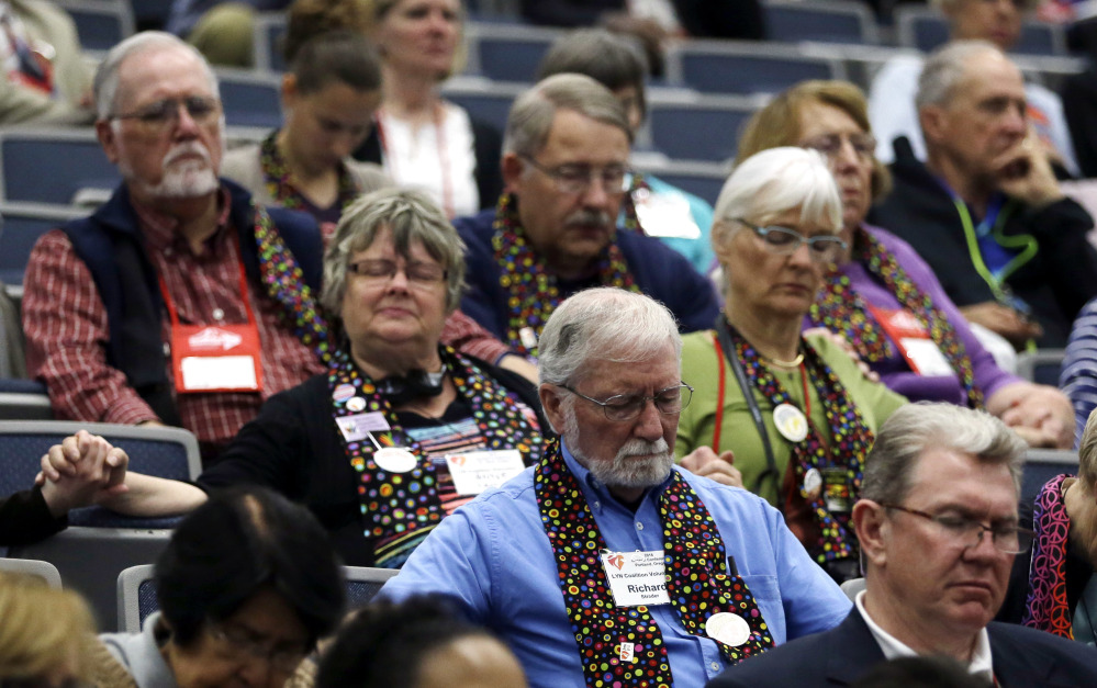 Attendees, many wearing multi-colored scarves in support of LGBT rights, pray after an unscheduled announcement from Bishop Bruce Ough, from the Dakotas-Minnesota church district and president of the Methodist Council of Bishops, concerning the stance of the Methodist church on LGBT rights during the United Methodist Church General Conference in Portland, Ore., Tuesday, May 17, 2016. The church currently bans same-sex marriages and the ordination of clergy who live openly with same-sex partners. (AP Photo/Don Ryan)