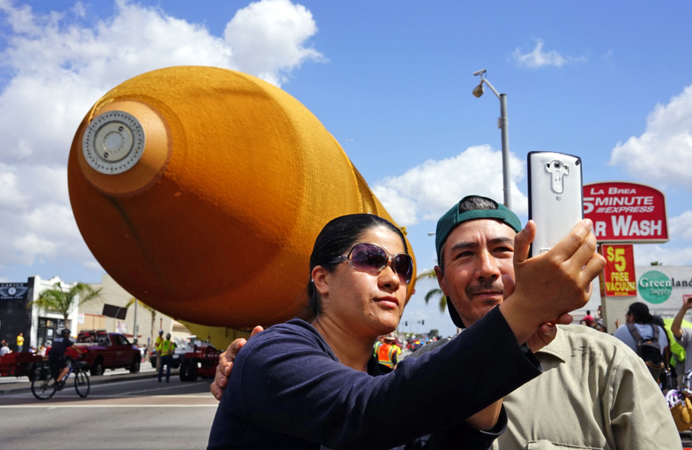 A couple takes a selfie as a massive space shuttle external fuel tank, the last one in existence, moves past on a street in Inglewood, Calif., en route from Marina Del Rey to the California Science Center in downtown Los Angeles on Saturday.