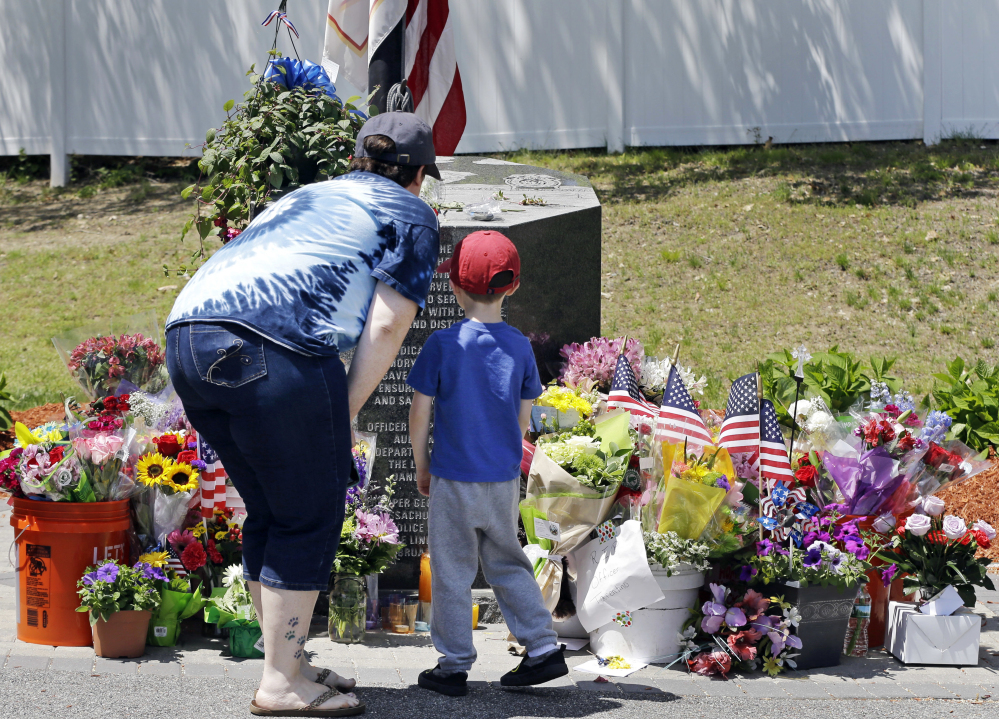 Danielle Dowd and her son Lucas pause before a memorial set up for slain Auburn police Officer Ronald Tarentino outside the police station in Auburn, Mass., on Monday. The man suspected of killing Tarentino during a weekend traffic stop had a lengthy criminal record.