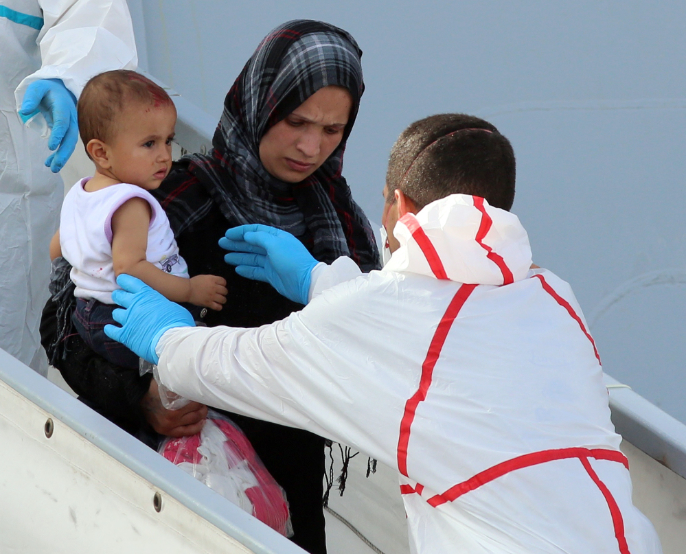 A woman disembarks with her baby from an Italian navy ship as it arrives at a Sicilian harbor Thursday. Improved weather conditions have led to an increase in the number of migrants risking the crossing from Libya.