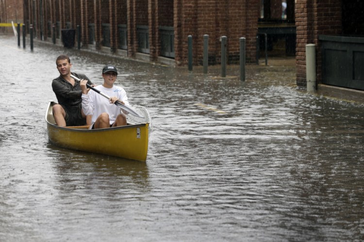 Dillon Christ, front, and Kyle Barnell paddle their canoe down a flooded street in Charleston, S.C., in 2015. During hurricane season, coastal living comes with significant risks.