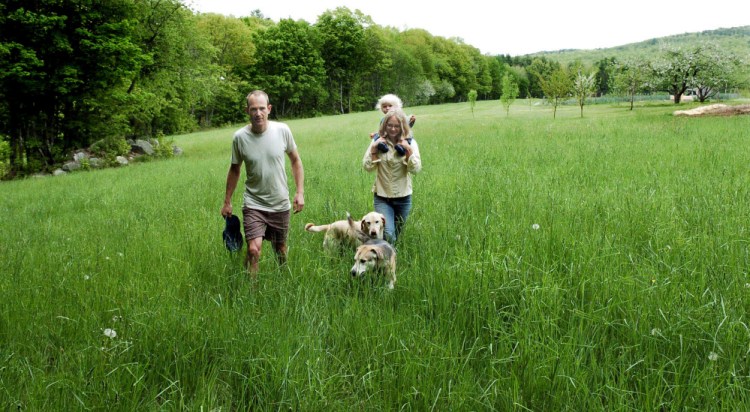 Marc and Lyra Collard, daughter Ara and dogs walk in a field in Norridgework, where they are establishing the Winding Hill Trails. The couple are opening the free public-access walking and running trails on their property with help from a New Balance Move More Kids grant.