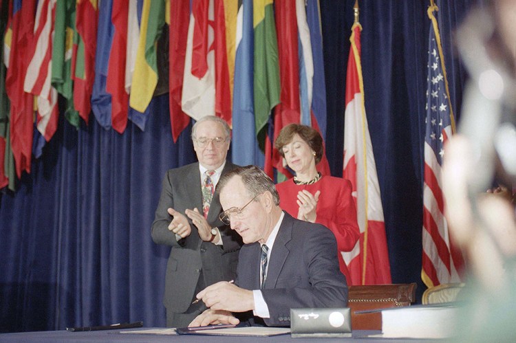 President George H. W. Bush signs the North American Free Trade Agreement during a ceremony at the Organization of American States headquarters on  Dec. 17, 1992, in Washington, D.C. Canadian Ambassador. Derek Burney and U.S. Trade Representative Carla Hills applaud. The president predicted an explosion of growth throughout North America as he signed the agreement. The Associated Press
