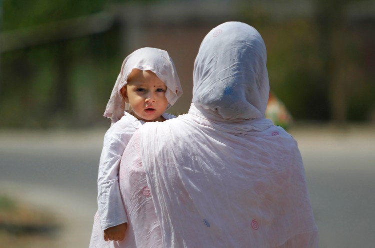 A mother and a child with his head covered with a wet towel, wait for transportation in Jammu, India, Thursday. Scorching summer temperatures are making life extremely tough for millions of people across northern and western India. The Associated Press