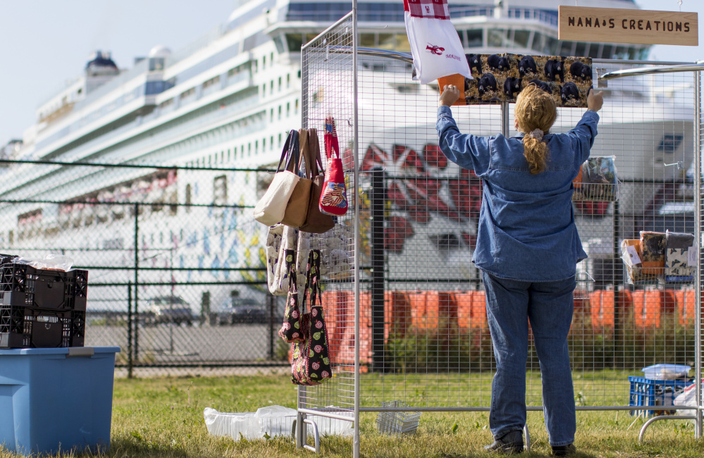 Joyce Whittemore of Carthage drapes some of the clothing and handbags she sells from her booth along the waterfront Thursday, with the Norwegian Gem looming in the distance. A city policy that took effect Wednesday restricts where street vendors can set up when cruise ships carrying more than 1,000 passengers visit Portland.