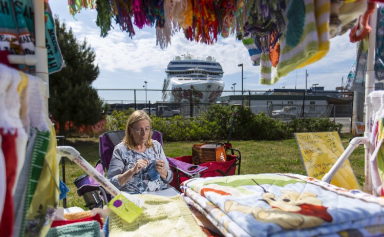With the Norwegian Gem docked at the Portland Ocean Terminal behind her, Donna Pradon of Wells sells hand-knit quilts and blankets Thursday. She and other street vendors say foot traffic is directed away from where they are now required to set up their booths.