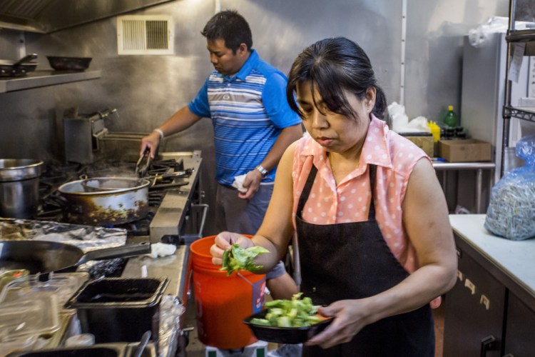 Siwaporn Roberts plates a takeout dish as her son, Ben Boonseng, finishes an appetizer on the grill in the kitchen of Thai Essan on Forest Avenue in Portland, the restaurant they own together.