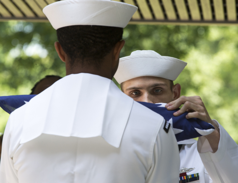 Petty Officer 2nd Class Dwight Merkle, right, prepares the ceremonial flag for presentation during the funeral  for World War II veteran Serina Vine