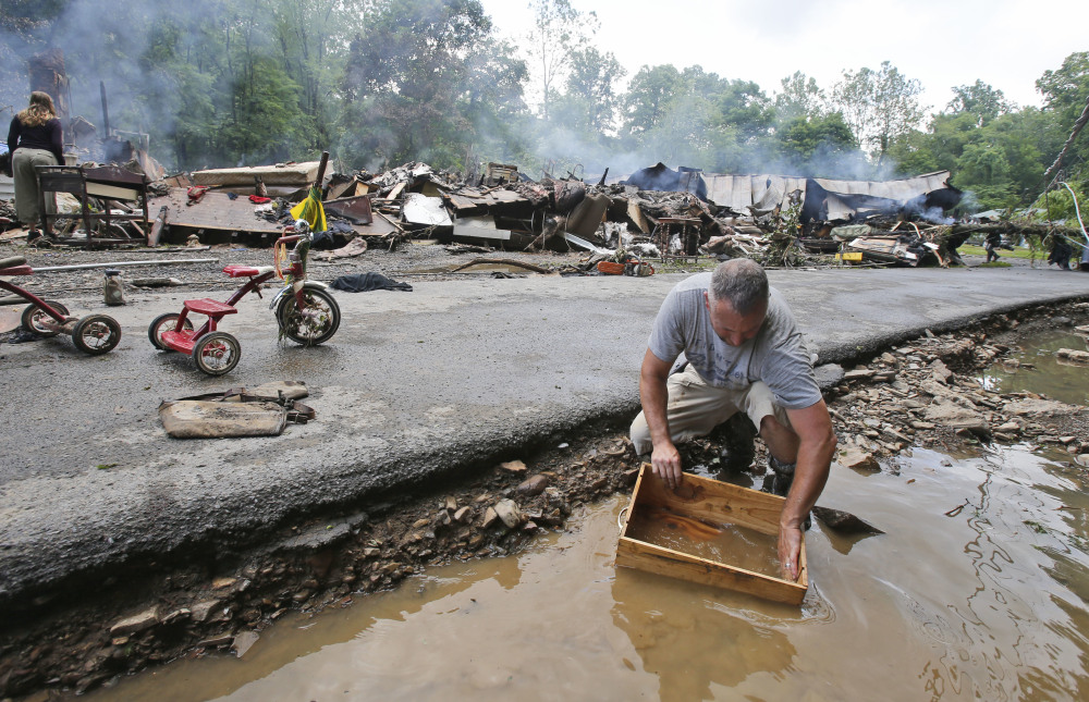Mark Lester cleans out a box with creek water as he cleans up from severe flooding in White Sulphur Springs, W.Va., on Friday.