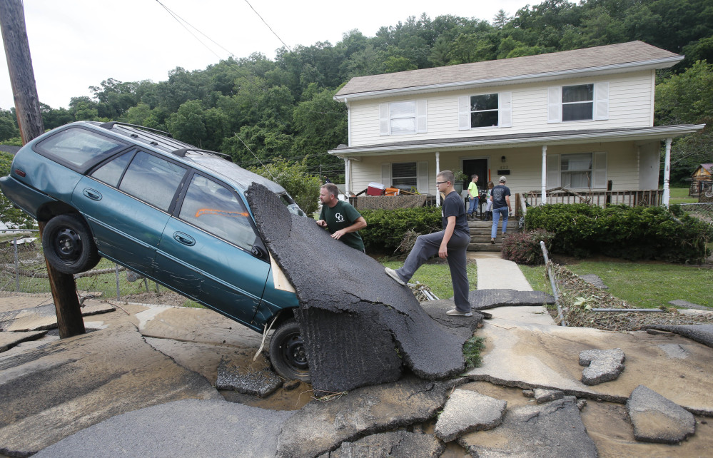 Jay Bennett, left, and stepson Easton Phillips survey the damage to a neighbor's car in front of their home, which was damaged by floodwaters, as the cleanup begins from severe flooding in White Sulphur Springs, W. Va., on Friday.