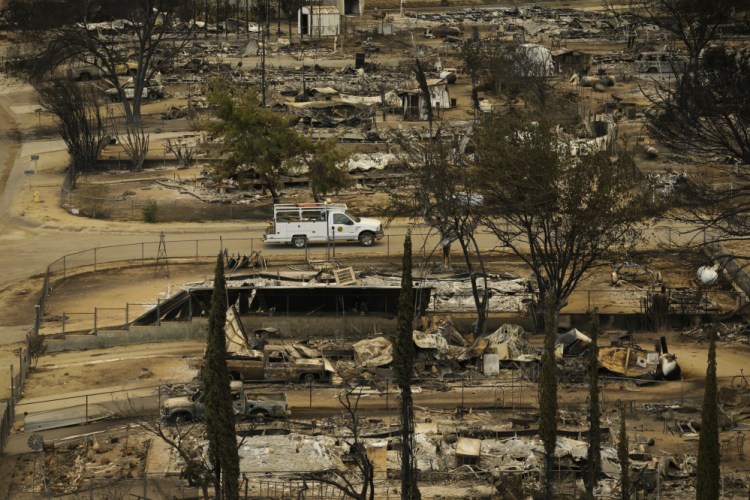 A pickup truck passes by the remains of mobile homes devastated by a wildfire, Saturday in South Lake, Calif.