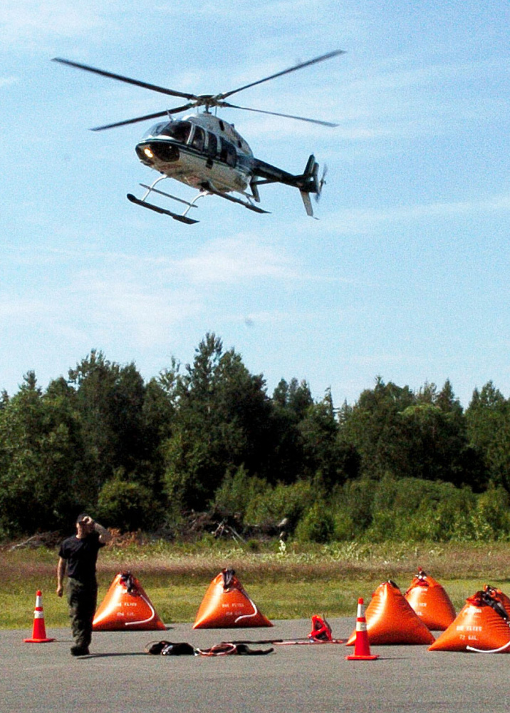 A Maine Forest Service helicopter lands at a command center at the Kingfield Fire Department as firefighters from the service and area departments battle a lightning-sparked fire on nearby Mount Abraham on Monday. The orange containers on the ground are portable tanks of water brought to the top of the mountain for firefighters.