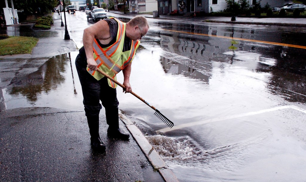 Madison Public Woks employee Bill Pierce clears a drain after a strong storm flooded Main Street on Monday afternoon.