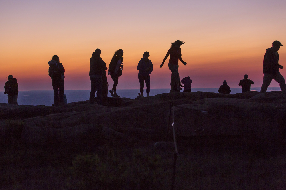 Visitors amble along the summit of Cadillac Mountain at dawn Monday. Acadia has been attracting ever-increasing crowds that some fear will threaten to fundamentally alter the experience of the park's natural beauty. "We don't want people stuck in traffic hunting endlessly for a place to park," said Kevin Schneider, park superintendent.