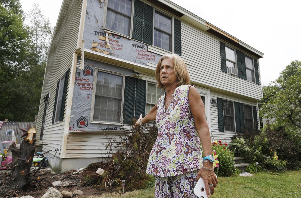 Julie Klippert stands Tuesday near the area of her house that was singed when a stray firework set a tree on fire. The stump of the tree, which had been removed, is at left.