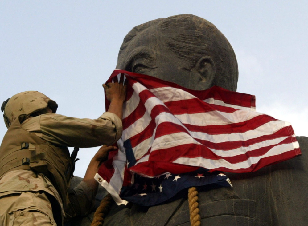 A U.S. Marine covers the face of a statue of Iraqi President Saddam Hussein – with a U.S. flag in Baghdad on April 9, 2003.