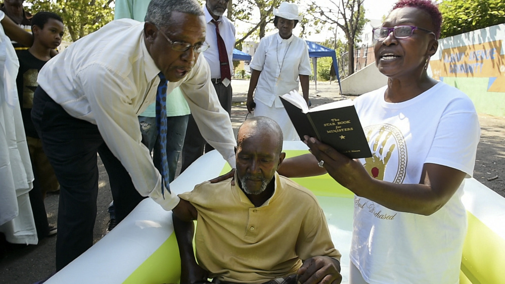 Pastor Gerald Miller, left, helps Pastor Lauri Andrews Malawitz support Willie Cannon as Malawitz prepares to baptize him in a small pool in Hartford, Conn., on June 26. Malawitz is the pastor of Effectual Fervent Prayer Outreach Ministries.
